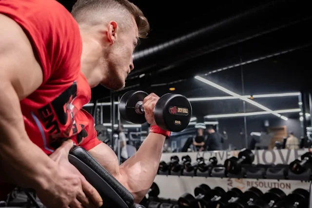 Homme en débardeur rouge exécutant une flexion des biceps à l'haltère en salle