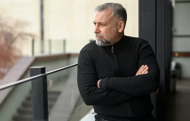 Homme d'une cinquantaine d'années, barbe grisonnante, bras croisés