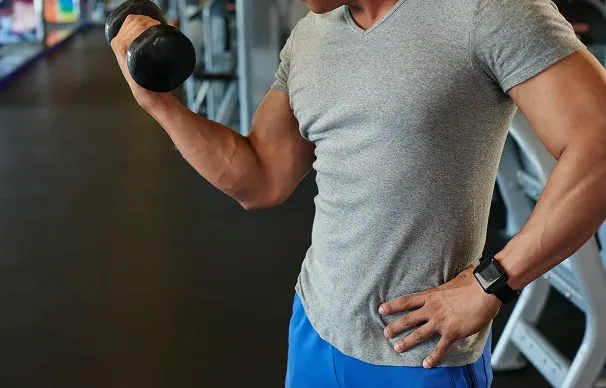 Homme réalisant un curl haltère en salle de sport