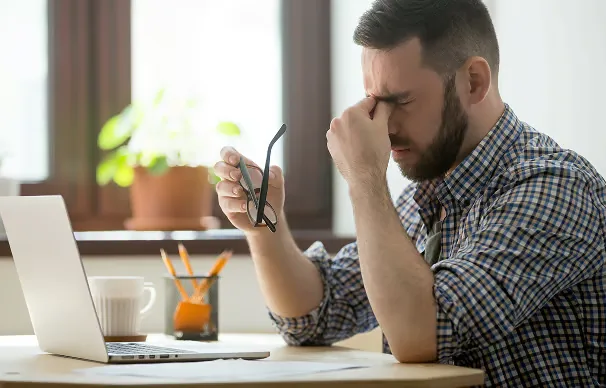 Homme fatigué devant son ordinateur portable, lunettes à la main