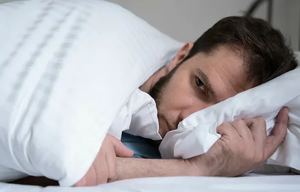 Homme allongé dans son lit, les yeux ouverts au milieu de la nuit